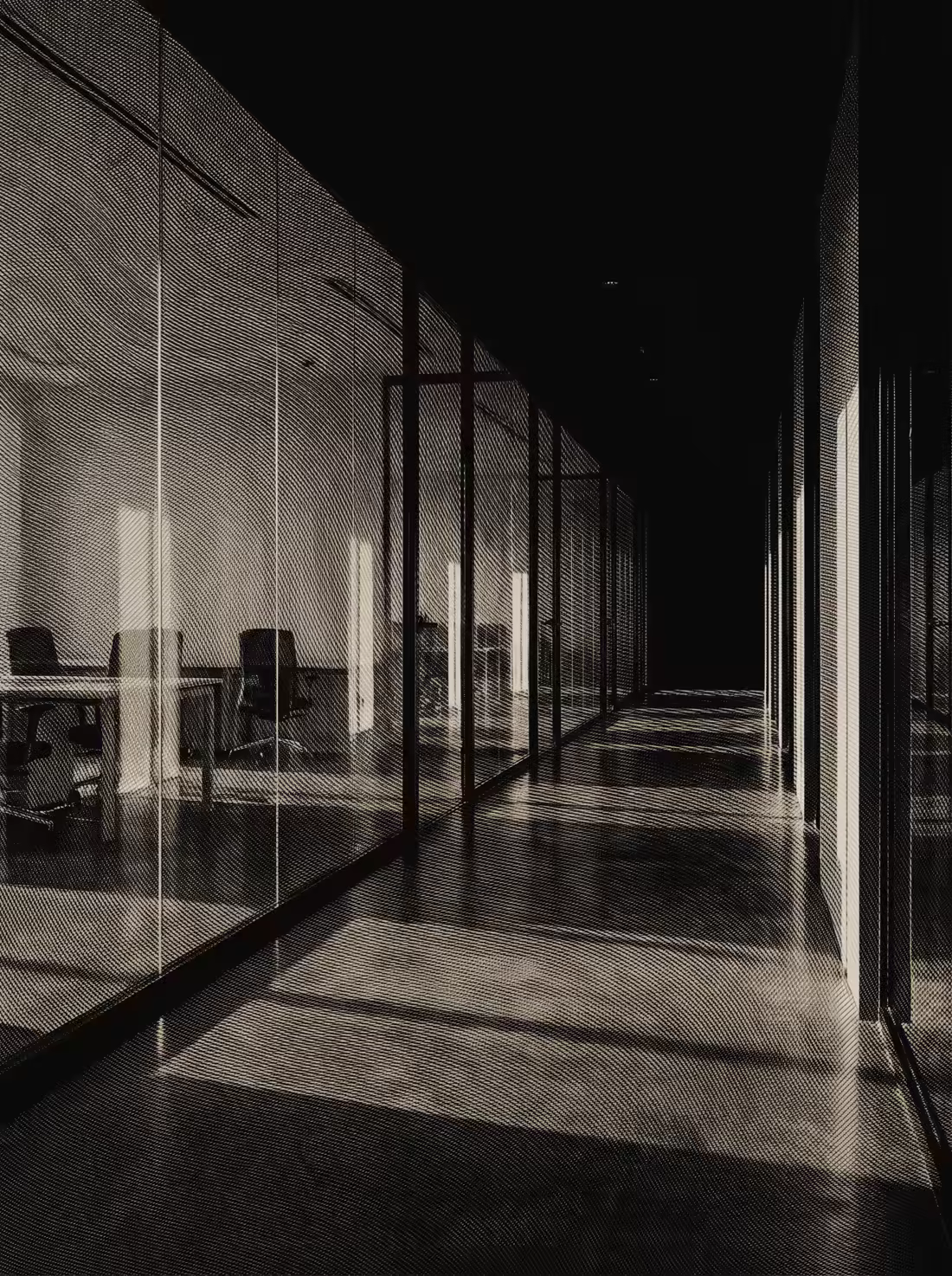 Un pasillo de oficinas vacío entre mamparas de cristal, con la luz rasante en el suelo.