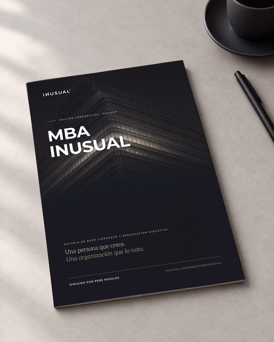 El dossier impreso del MBA INUSUAL, edición corporativa, sobre un escritorio claro con luz natural, junto a una taza y un bolígrafo